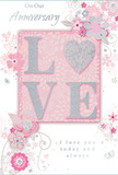 The photograph shows a softly romantic anniversary card that blends pastel pinks and silvery greys to create an atmosphere of treasured intimacy. At its centre, the word LOVE is prominently displayed in raised, glittered letters, the surface dusted with fine, light-catching particles that give a gentle shimmer rather than a bold sparkle. The letter O is replaced by a silver heart, slightly more textured and metallic in appearance, forming a small but striking focal point that symbolises shared devotion. Encircling this central motif, delicate blooms in blush and mauve unfold along curling stems, drawn with a watercolor-soft touch that suggests the airy grace of an English spring garden in Surrey-perhaps reminiscent of blossoms seen near Box Hill or along the River Wey. Fine lines and flourishes curl between petals, accompanied by tiny swirls, scattered petals, and a few subtle butterflies that bring a sense of movement and whimsy to the layout. The background sits in a gentle powder pink, keeping the tone warm and intimate while allowing the silver accents and floral artwork to stand out clearly. Scripted text, including On Our Anniversary and I love you today and always, is rendered in an understated, elegant calligraphy, echoing the natural curves of the vines and leaves. Together, the elements create a composition that feels like a quiet celebration of a shared journey, ideal to accompany an anniversary bouquet delivered to a cosy home or romantic dinner setting anywhere in Surrey.